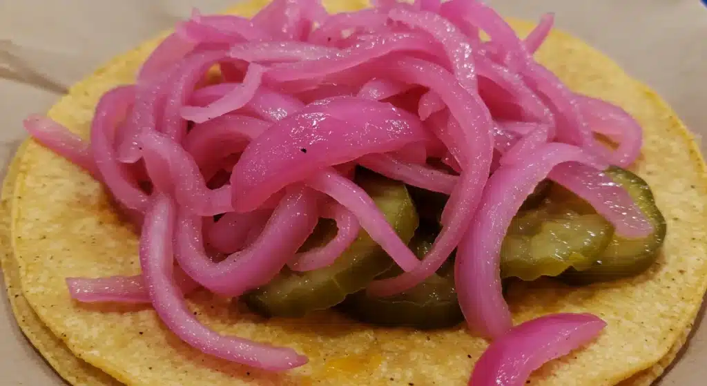 Pickled red onions adding crunch and acidity to tacos with grilled meat and cilantro
